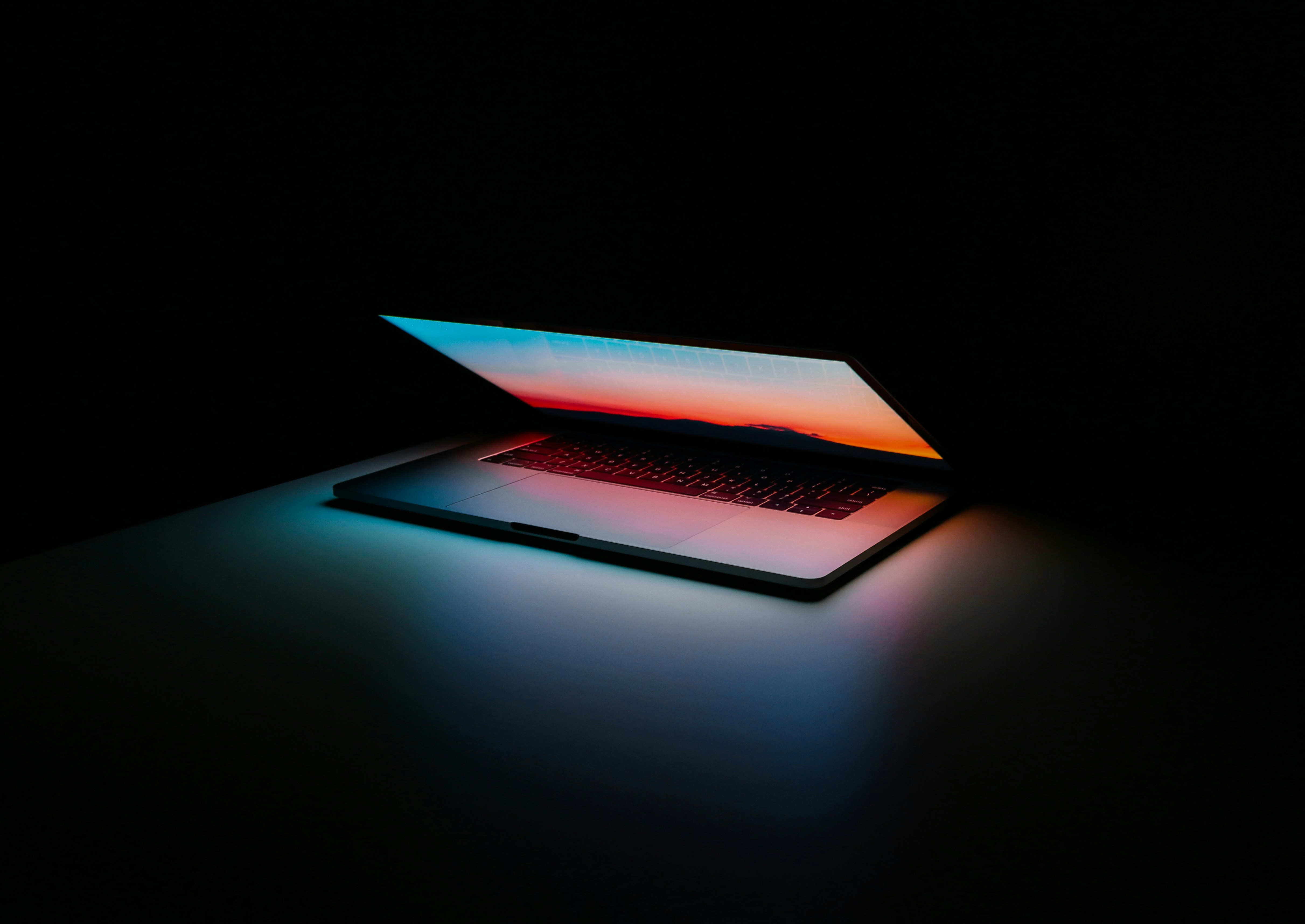 An open laptop illuminated by blue and red light in a dark room.